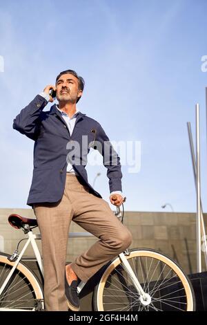 Adult male sitting talking on the phone with bicycle leaning against the wall. Ecological transport concept. High quality photo Stock Photo
