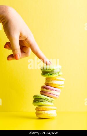 Female hand holding tasty macaroons on yellow Stock Photo
