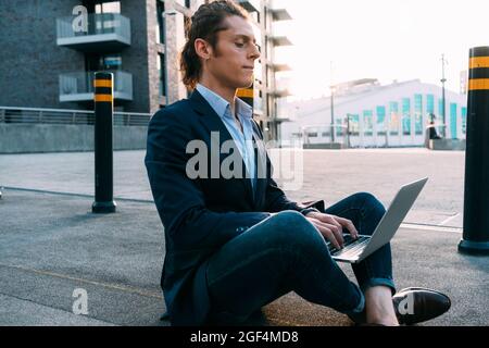 Businessman using laptop while sitting cross-legged on footpath Stock Photo