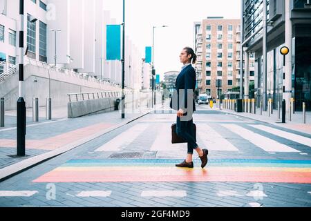 Businessman holding briefcase while walking on multi colored road markings in city Stock Photo