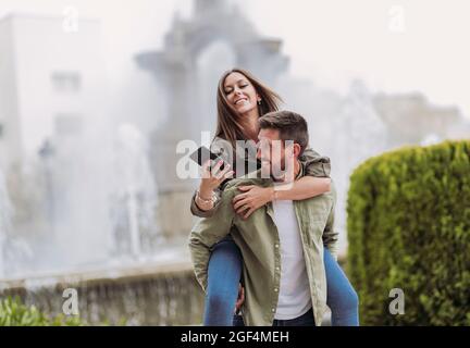 Smiling woman using mobile phone while piggybacking on boyfriend Stock Photo