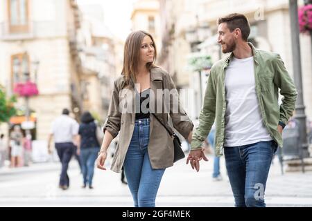 Couple holding hands while walking on city street Stock Photo