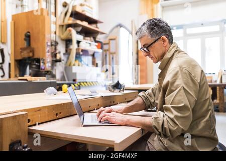 Mature male carpenter working on laptop in workshop Stock Photo