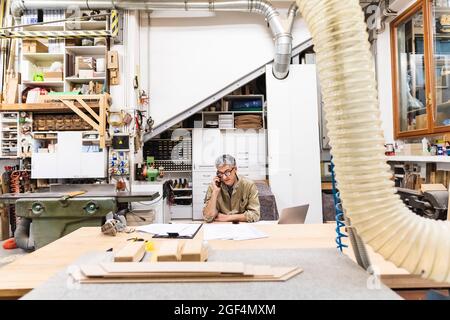 Mature male carpenter talking on smart phone in workshop Stock Photo