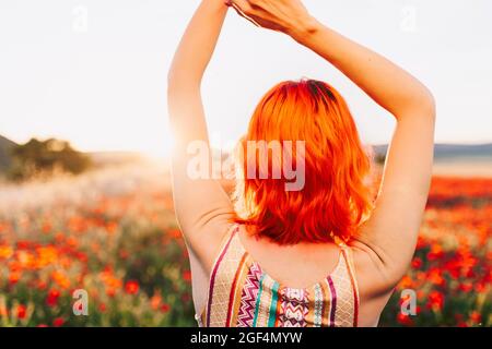 Redheaded woman with hands raised at sunset Stock Photo