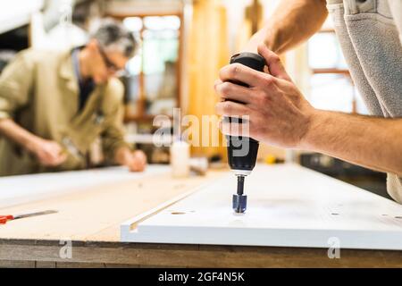 Male carpenters using drill machine on plank at workshop Stock Photo