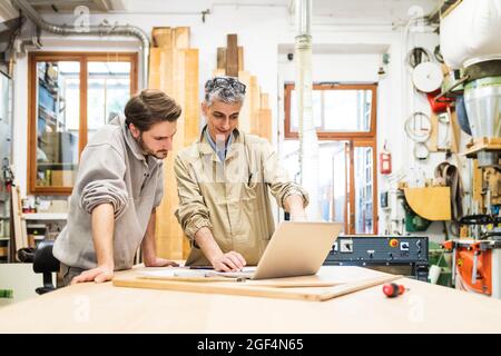 Mature male owner discussing with colleague over laptop at workshop Stock Photo