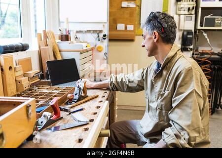 Male craftsperson using laptop on table at workshop Stock Photo