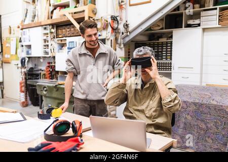 Mature male owner using virtual reality simulator while colleague standing in workshop Stock Photo