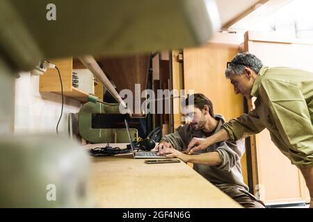 Mature male owner discussing with colleague over laptop at workshop Stock Photo