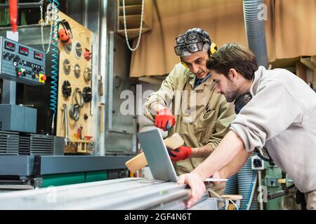 Male mature craftsperson discussing over laptop at workshop Stock Photo