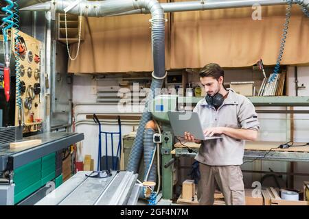 Male owner using laptop while standing at workshop Stock Photo