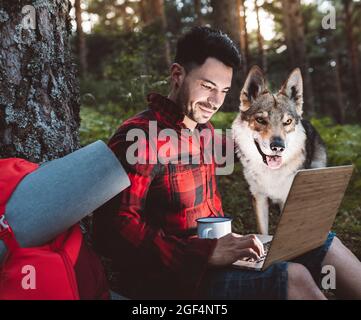 Mid adult man working through laptop while sitting with dog in forest Stock Photo