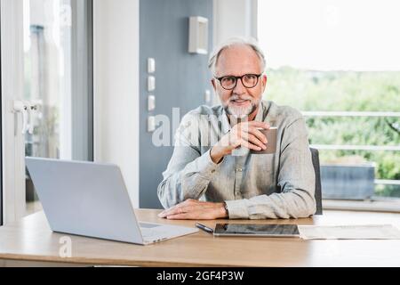 Businessman with eyeglasses holding mug at desk in home office Stock Photo
