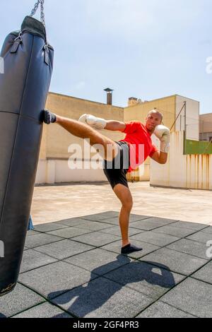 Muscular man punching with leg a boxing bag on cross fit training at the outdoors. Training concept Stock Photo