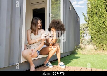 Female friends having wine while sitting at doorway of house Stock Photo