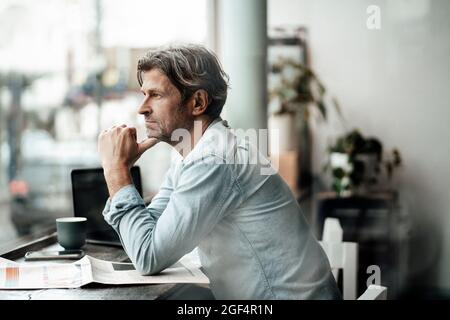 Thoughtful man sitting with newspaper looking through window while sitting in cafe Stock Photo