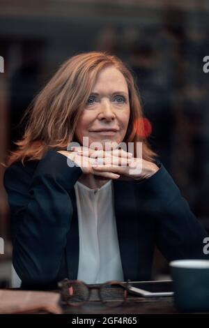 Thoughtful blond businesswoman sitting with hand on chin in cafe Stock Photo
