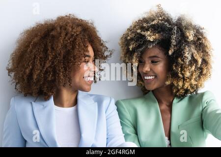 Smiling female colleagues looking at each other in front of white wall Stock Photo
