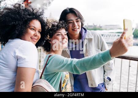 Smiling woman taking selfie with male and female friends Stock Photo
