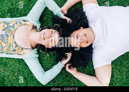 Young female friends with hands in hair lying on grass in public park Stock Photo