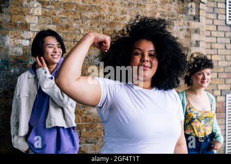 Young woman flexing muscle with male and female friends in background Stock Photo