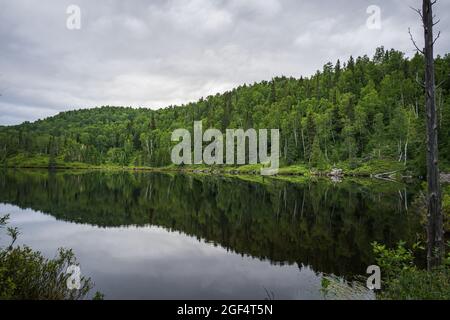Reflections on a cloudy day in the waters of the small Lac des Pères at the beginning of Pic de la Tête de Chien hiking trail in Monts Valin National Stock Photo