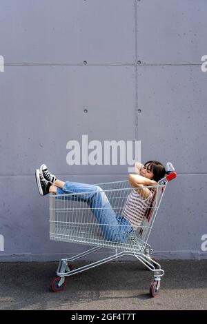 Woman sleeping in shopping cart on footpath Stock Photo