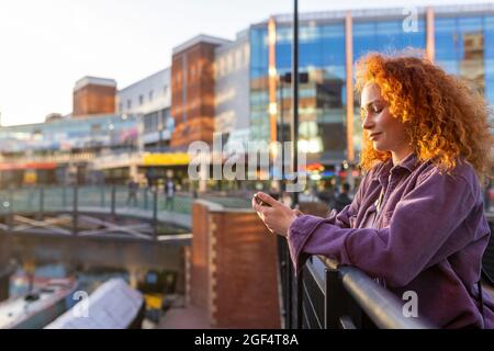 UK, Birmingham, redhead woman using smartphone in the city at sunset Stock Photo