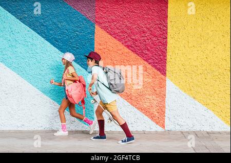 Girl and boy with backpacks walking on footpath Stock Photo