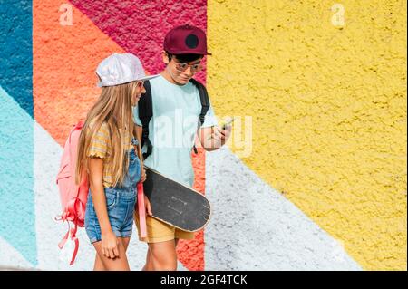 Boy using mobile phone while sitting by female friend on footpath Stock Photo