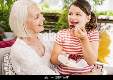 Granddaughter eating cake while sitting with grandmother at balcony Stock Photo
