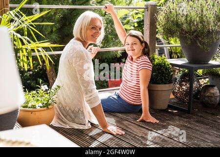 Smiling woman sitting with girl at balcony Stock Photo