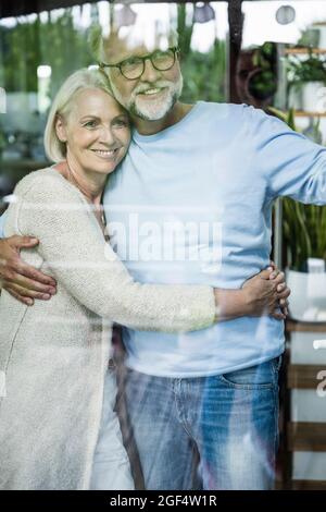 Smiling couple standing seen through glass window Stock Photo