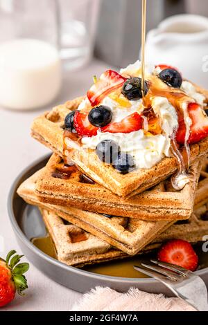 Maple syrup pouring on stack of fresh waffles with blueberries, strawberries and ice cream Stock Photo
