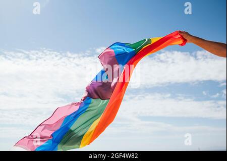 Happy gay man gesturing while waving rainbow flag during sunny day Stock Photo