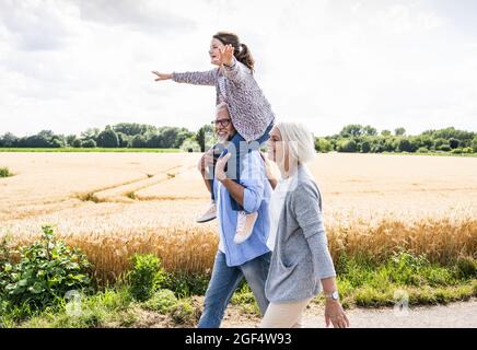 Grandparents walking with playful granddaughter during sunny day Stock Photo