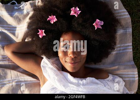 Smiling young woman with pink flowers on Afro hair Stock Photo