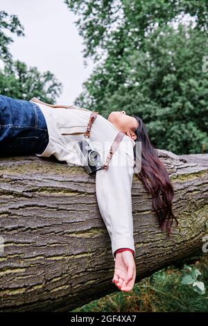 Carefree woman lying on fallen tree in public park Stock Photo