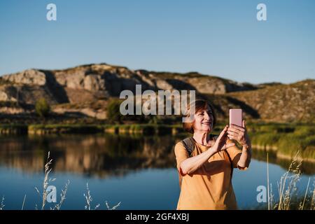 Senior woman taking selfie through smart phone near lake Stock Photo