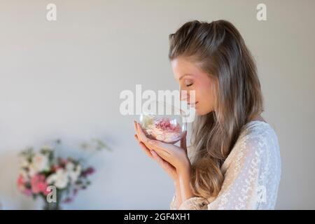 Beautiful young woman smelling scented roses in terrarium bowl Stock Photo