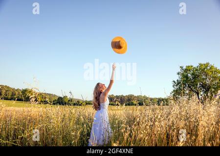 Happy young woman throwing hat while standing in field Stock Photo