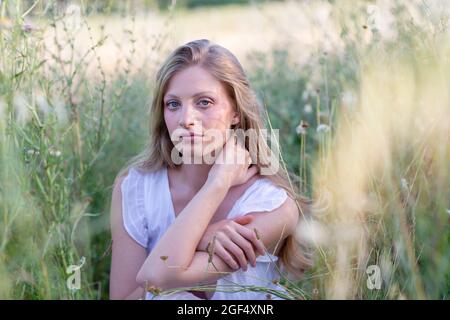 Beautiful young woman sitting amidst grass in field Stock Photo