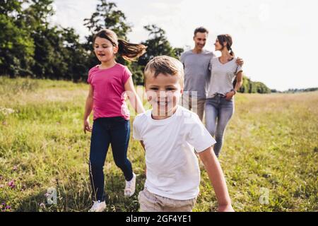 Boy with sister running while parents walking on meadow Stock Photo