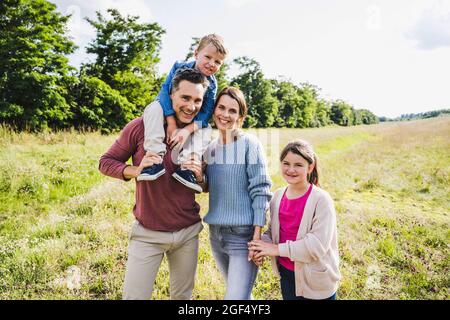 Man carrying boy on shoulders while standing with woman and daughter at meadow Stock Photo