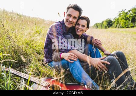 Smiling couple sitting together by guitar on grass Stock Photo