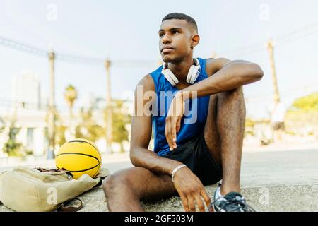 Young male basketball player looking away while sitting at sports court Stock Photo
