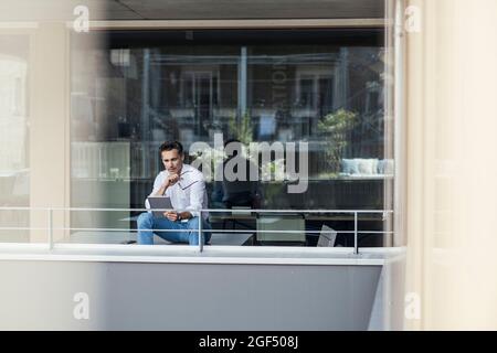 Thoughtful businessman using digital tablet while sitting at office balcony Stock Photo