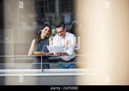 Male and female colleagues checking document while standing at office balcony Stock Photo