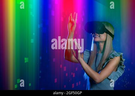 Happy woman with virtual reality simulator gesturing over multi-colored background Stock Photo